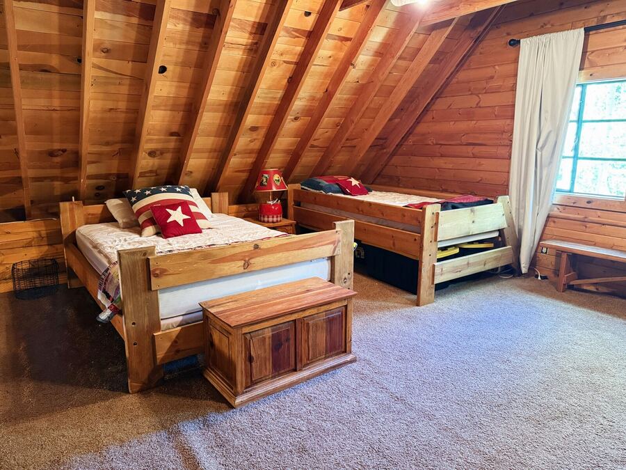 Bright loft bedroom with a log bed and a twin bed under the sloped pine ceiling