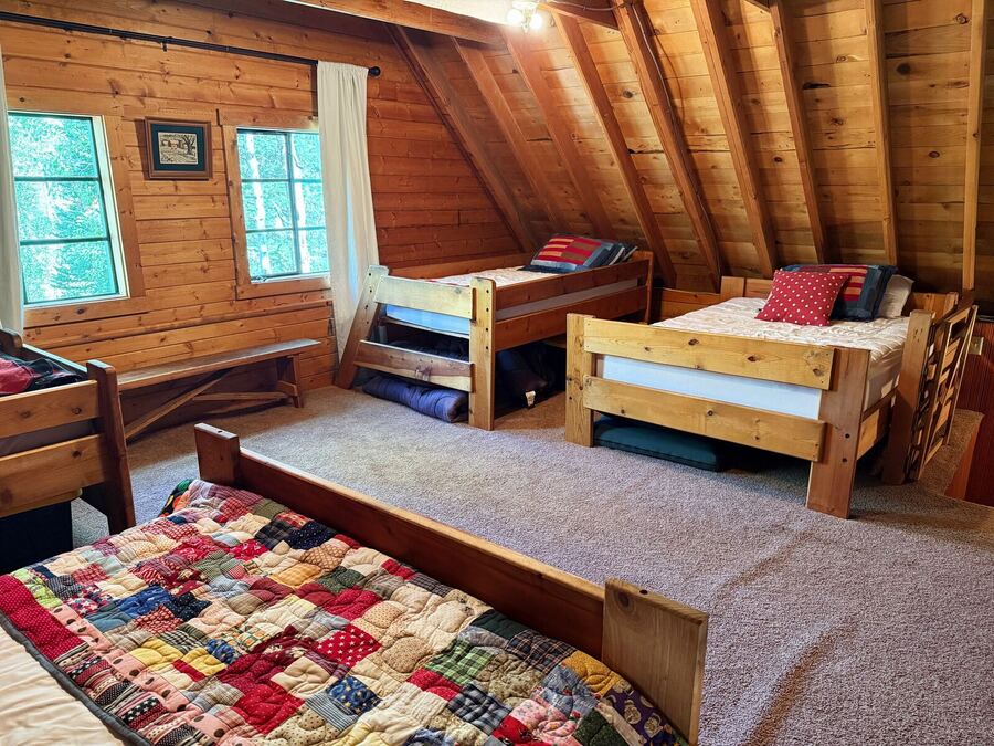 Loft room with several beds, windows along the wall and a patchwork quilt